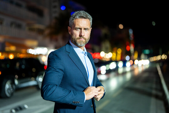 Successful businessman posing at night city. Rich businessman in a suit standing in the night street. Handsome businessman in a formal suit. Stylish businessman. Elegant business man. - Powered by Adobe