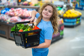 Kid with shopping cart in grocery store. Child choosing fresh vegetables. Cute boy shopping for...