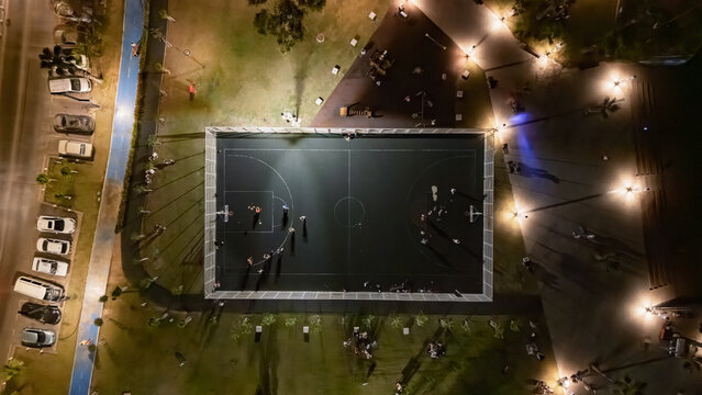 Aerial drone view of people playing basketball in city court, illuminated basketball playground at night, sports grounds for outdoor fitness