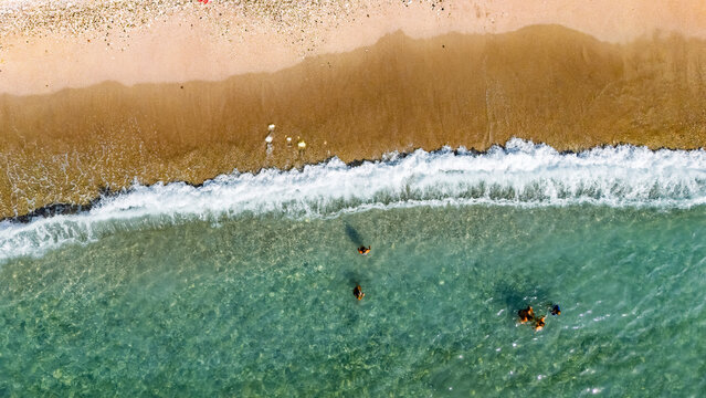 Aerial drone view of sandy beach and turquoise sea waves with people sunbathing, swimming and relaxing, holiday vacation concept, Antalya Konyaalti beach, Turkey