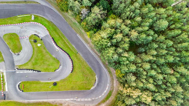 Aerial drone view of karting race track in green forest with racing go-karts cars driving, kart racing open wheel motorsport