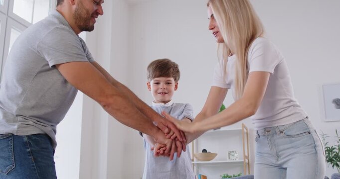 Happy family friendly motivated team, parents and son raise common high fives on briefing after finding problem solution, successful result, unite hands above to celebrate common achievement and unity