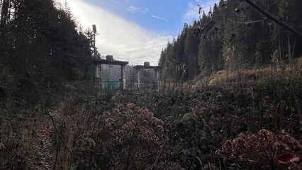 Abandoned concrete water dam structure in a forest, moss-covered walls and rusty railings reflecting in calm water, eerie and post-apocalyptic atmosphere.