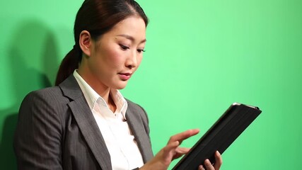 Professional Asian businesswoman in a suit using a digital tablet with a green screen background ideal for technology and business concepts. - Powered by Adobe