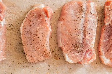 fresh pork chops seasoned with salt and pepper on parchment paper