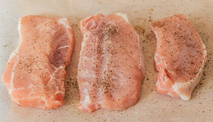fresh pork chops seasoned with salt and pepper on parchment paper