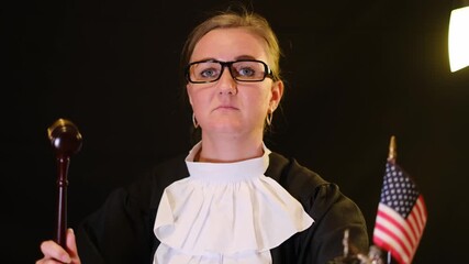 Female judge in traditional robe lifting a wooden gavel at the courtroom desk with American flag - Powered by Adobe