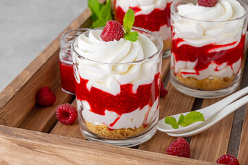 Raspberry trifle with whipped cream, berry sauce, cookie crumbs and mint leaves in a glass on a wooden tray. Summer diet dessert.