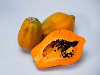Still life of two whole papayas and one sliced papaya on a plain background conveys freshness.