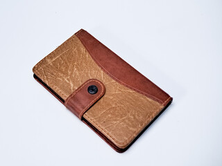 A brown and tan leather journal or book with a strap closure lies on a white surface studio shot.