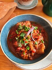 Traditional meat stew with tomato sauce, herbs, and spices served in a blue bowl with flatbread. Delicious homemade comfort food, perfect for restaurant, or culinary concept visuals.