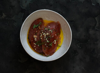 Raw turkey breast marinated in spices and olive oil for baking, barbecue, grilling in a bowl on a dark background, top view