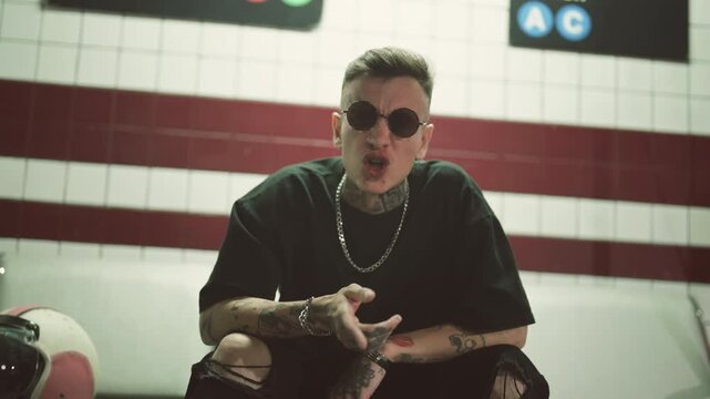 Hip-hop singer performing trendy rap song in underground interior, portrait indoors. Self-expression and individuality, be yourself and make your art, tattoos on face and body of stylish male person