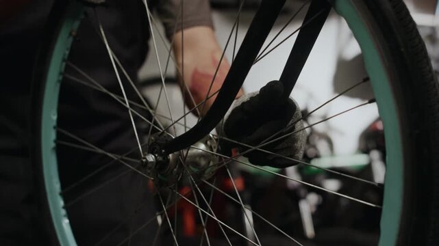 Unrecognizable repairman attaching wheel to bicycle fork while repairing it in workshop
