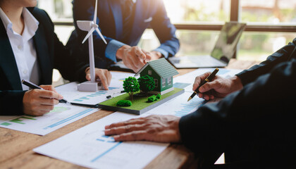 Professionals discussing sustainable and eco-friendly real estate projects, with a model house and wind turbine on the table.