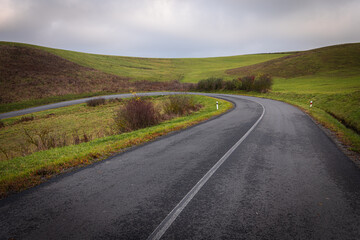 Curving rural asphalt road in green hills with no-passing road marking. Dangerous blind curve in the countryside on an overcast day.