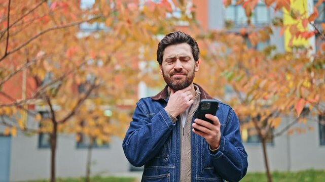 Throat discomfort experienced outdoors by an individual using a smartphone. Expresses feelings of illness and concern in an autumn setting. Prioritizes health and digital communication.
