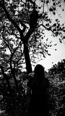 Black and white image of a person standing under a tree looking at the sky