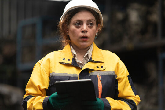 Hispanic female foreman worker standing holding tablet, checking inventory of auto parts and engine maintenance duties in factory.