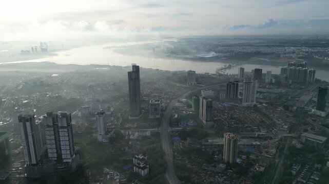 A city with a river in the background. The sky is cloudy and the city is covered in smoke. Aerial view Johor Bahru, Johor