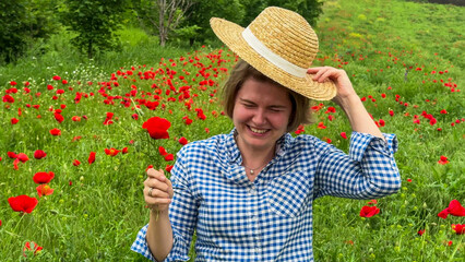 Smiling Caucasian woman in gingham shirt and straw hat amidst scarlet poppy field, capturing tranquil essence of World Laughter Day