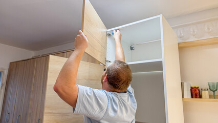 A Caucasian man meticulously assembles a cabinet, celebrating DIY Day and International Handyman Appreciation Week