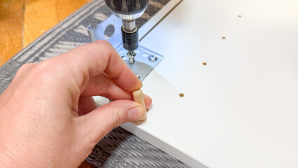 Hand of Caucasian woman assembles furniture with dowel and drill, evoking DIY triumph, reminiscent of National Craft Month