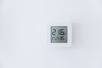 The thermostat displays the temperature in Celsius and the humidity in the room. Smart home device on a white wall