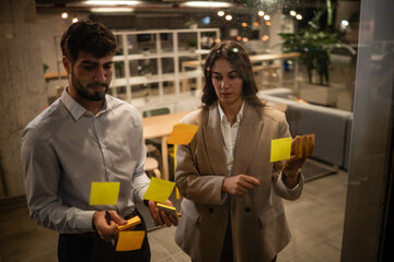 Business colleagues brainstorming ideas using sticky notes on glass wall