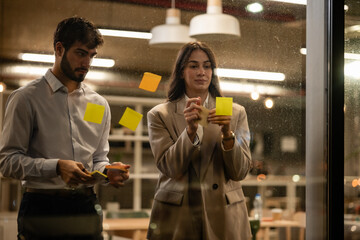 Business colleagues brainstorming ideas using sticky notes on glass wall
