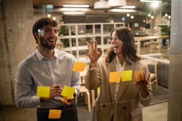 Colleagues brainstorming ideas on glass wall with sticky notes
