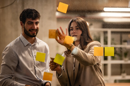 Colleagues brainstorming new ideas using sticky notes on glass
