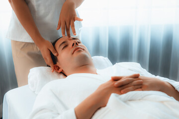 Caucasian man enjoying relaxing anti-stress head massage and pampering facial beauty skin recreation leisure in dayspa modern light ambient at luxury resort or hotel spa salon. Quiescent