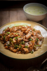 Delicious Thai-style fried chicken with rice, topped with crispy garlic and herbs, served with a bowl of clear soup on a wooden table. Authentic homemade Asian meal, beautifully presented for traditio