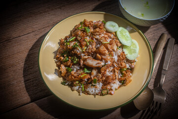 Delicious Thai-style fried chicken with rice, topped with crispy garlic and herbs, served with a bowl of clear soup on a wooden table. Authentic homemade Asian meal, beautifully presented for traditio