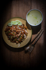 Delicious Thai-style fried chicken with rice, topped with crispy garlic and herbs, served with a bowl of clear soup on a wooden table. Authentic homemade Asian meal, beautifully presented for traditio