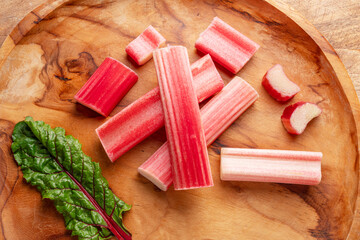 Cuts of red rhubarb stem on wooden plate on the table, top view.