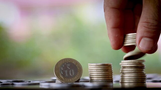 Young Man&rsquo;s Hands Stacking Growing Piles of Indian Rupee Coins with Standing 10 Rupee Coin