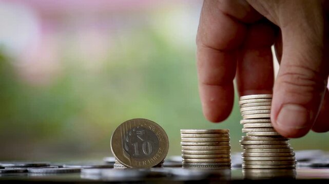Young Man&rsquo;s Hands Stacking Growing Piles of Indian Rupee Coins with Standing 10 Rupee Coin