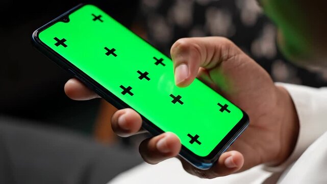 Close up of a hand holding a smartphone with a green screen and tracking markers, perfect for digital content and app demonstrations.