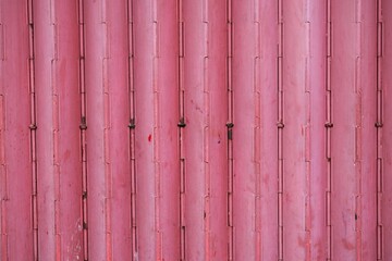 Close-up of a pink painted metal folding gate, showing vertical ridges and subtle signs of wear and urban use.