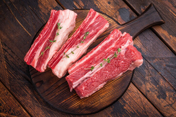 Raw beef short ribs with thyme and pink peppercorns on a dark wooden cutting board. Excellent for a BBQ recipe or restaurant menu.