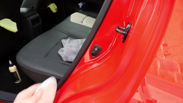Close up hand polishing a door shut jamb on a red car with white microfibre pad