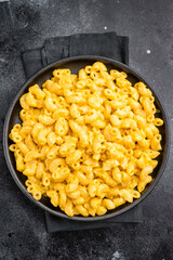 Golden mac and cheese in a black skillet, rustic dark background, fork beside