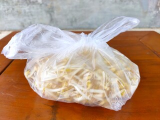 A clear plastic bag filled with fresh bean sprouts on a wooden table. Fresh produce from a local market in Malang, Indonesia.