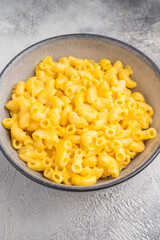 Creamy macaroni and cheese in a rustic bowl on a wooden board, set against a textured gray background