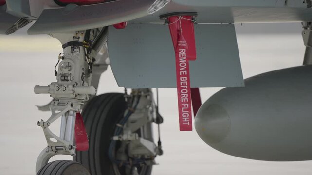 Close-up of military jet landing gear with red remove before flight tag and external fuel tank