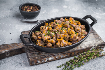Fried chicken hearts with carrot and herbs in cast iron pan on gray concrete background perfect for food photography.