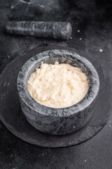 Dark and moody food photo. Creamy horseradish sauce in a marble mortar and pestle, set on a textured slate background. Copy space.