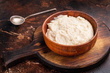 Overhead shot of rich white condiment (aioli or horseradish) in a bowl on a dark textured wood surface. Gourmet serving style.